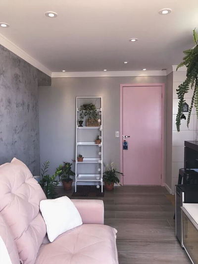 Sala com sofá rosa, porta rosa e parede de cimento queimado