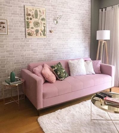 Sofá rosa bebe com almofadas e parede com papel de parede de tijolinho cinza