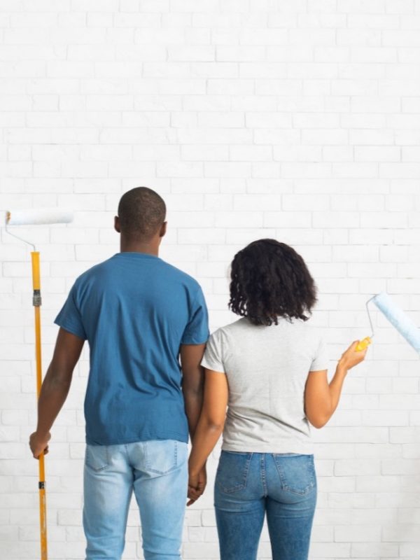 Casal olhando para a parede com rolos de pintura