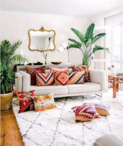 Decoração de sala com tapete, sofá com almofadas coloridas e planta grande