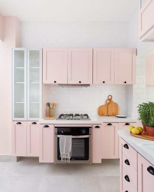 Cozinha com armários rosa e azulejo branco. Fogão embutido, cooktop e acessórios de cozinha na bancada.